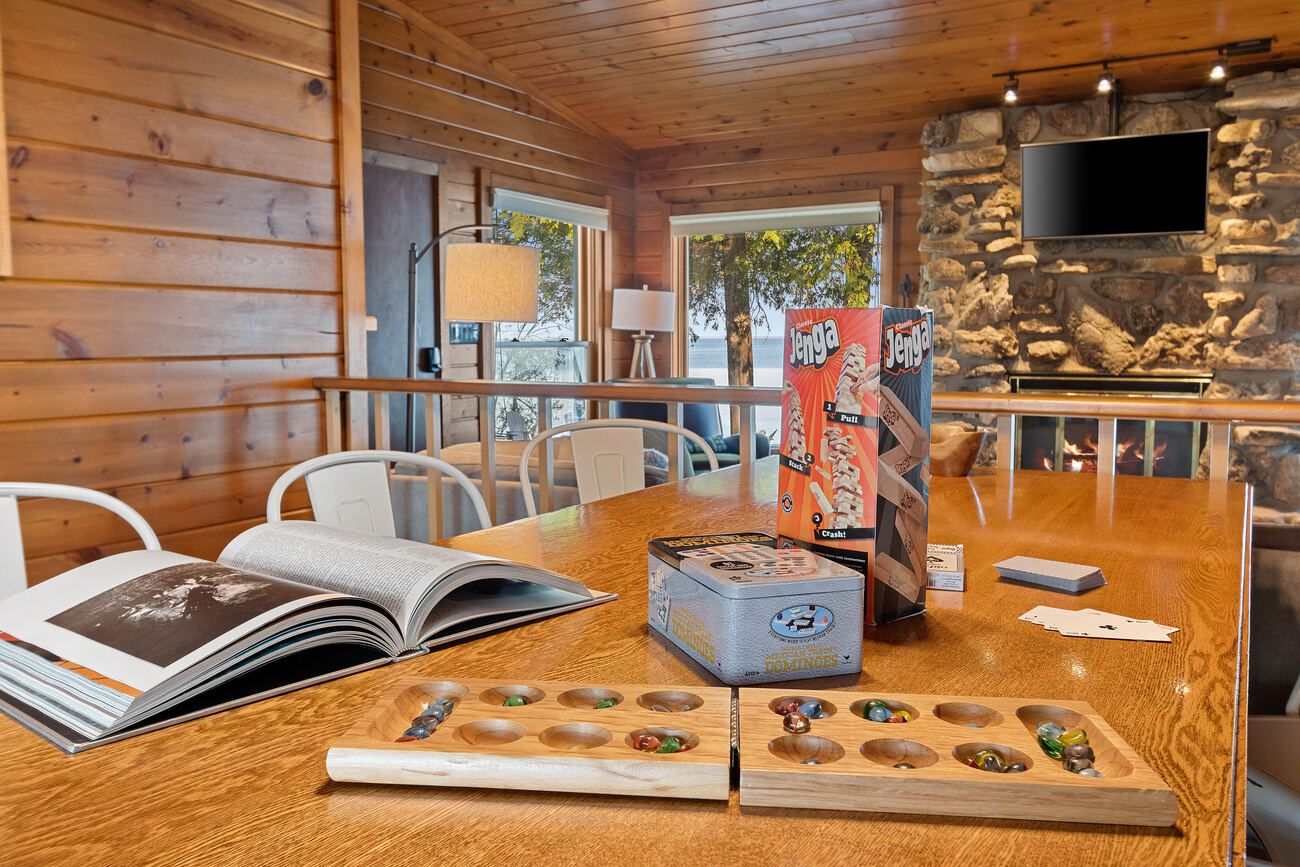 Cottage interior — game table stocked with Jenga, dominoes, and mancala in front of a stone fireplace